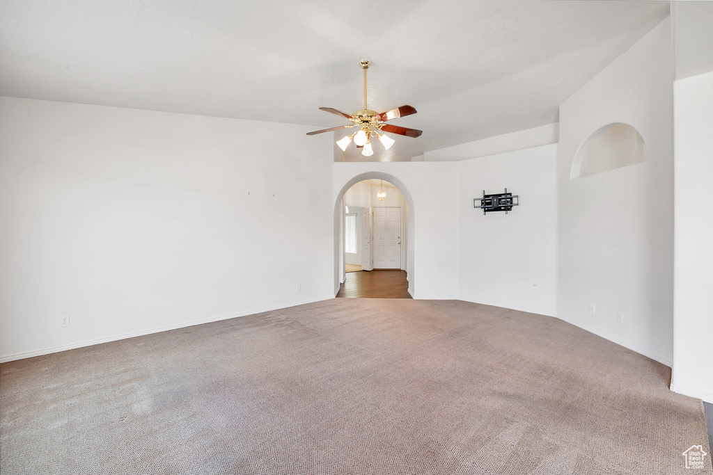 Carpeted spare room featuring vaulted ceiling, ceiling fan, and arched walkways