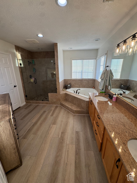 Full bathroom with a textured ceiling, a shower stall, a garden tub, double vanity, and wood finished floors