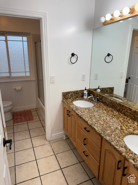Bathroom with toilet, baseboards, a sink, tile patterned flooring, and double vanity