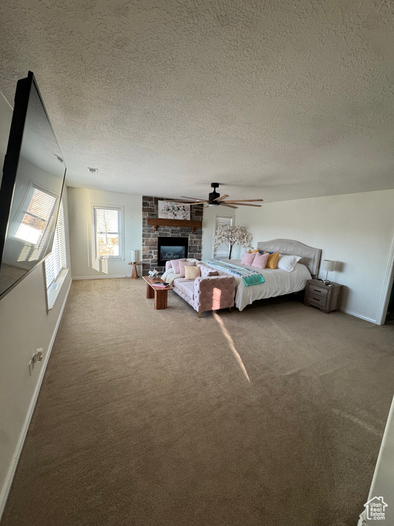 Carpeted bedroom featuring baseboards, a glass covered fireplace, a ceiling fan, and a textured ceiling