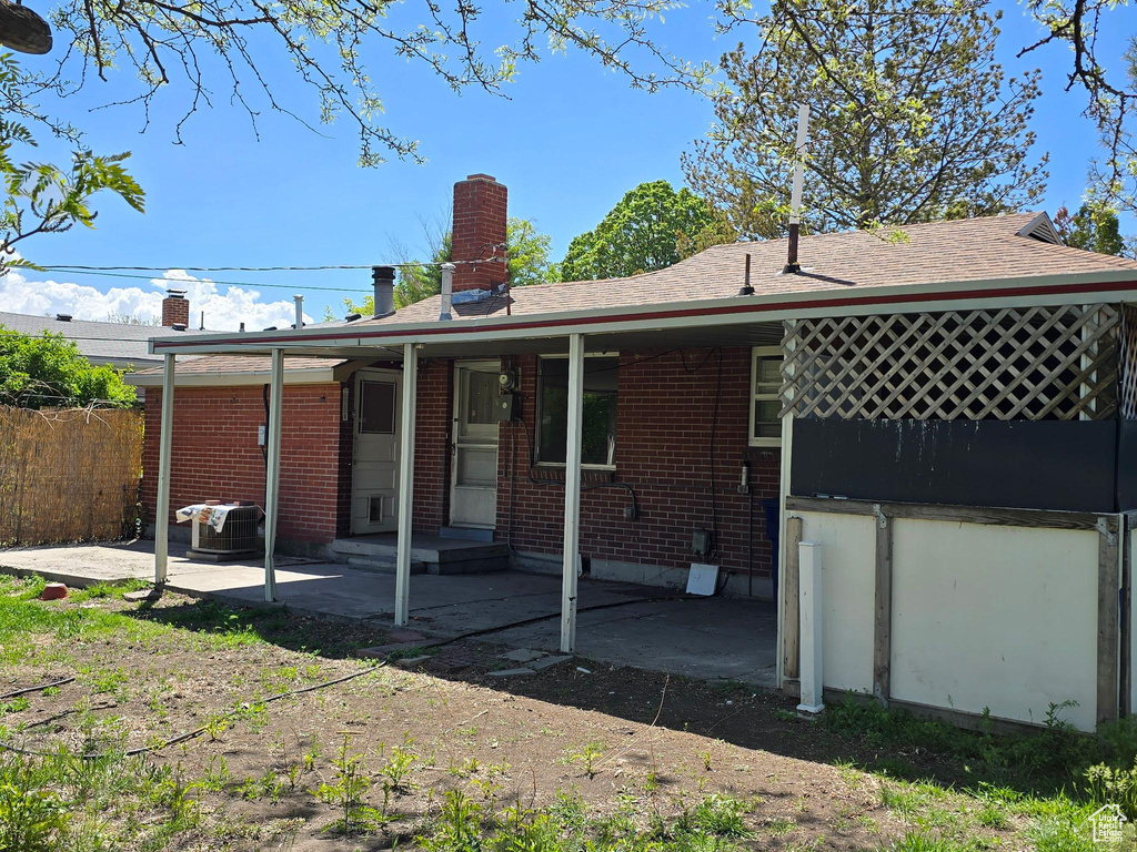 Back of property with fence, brick siding, a patio, central AC unit, and a shingled roof