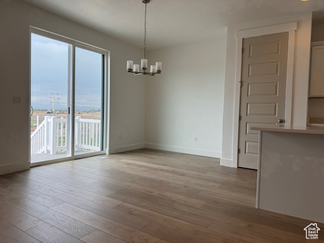 Unfurnished dining area with an inviting chandelier, hardwood / wood-style flooring, and baseboards