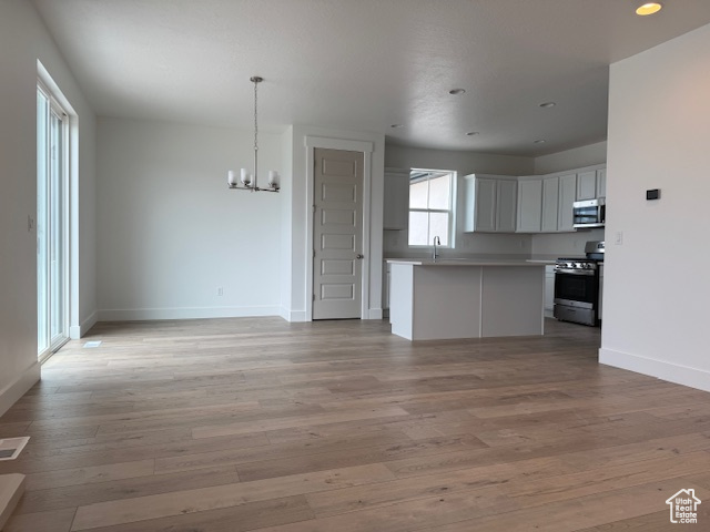 Unfurnished living room featuring an inviting chandelier, light wood-type flooring, baseboards, and a sink