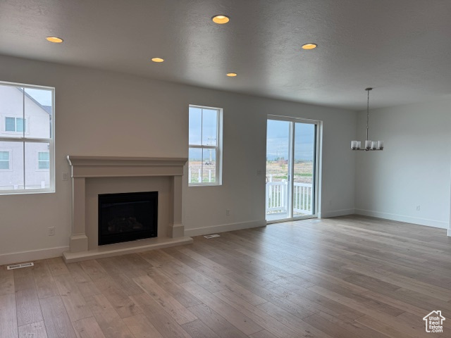 Unfurnished living room with hardwood / wood-style flooring, a fireplace with raised hearth, visible vents, an inviting chandelier, and baseboards