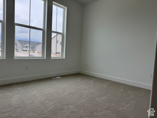 Carpeted empty room featuring a wealth of natural light, baseboards, and visible vents