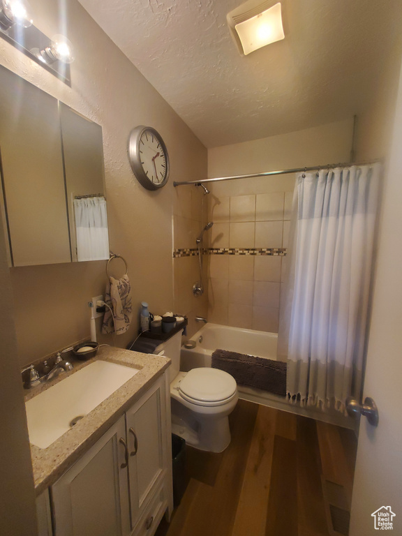 Full bathroom with a textured ceiling, toilet, shower / tub combo with curtain, vanity, and wood finished floors