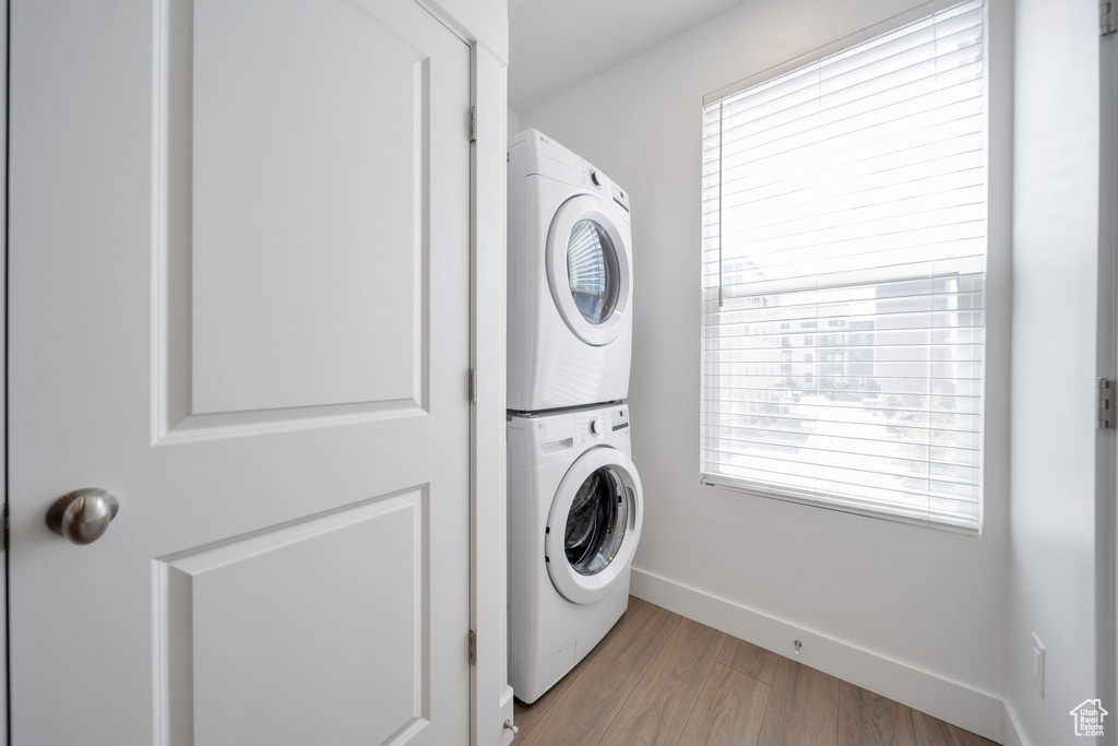 Clothes washing area with stacked washer / dryer, laundry area, a healthy amount of sunlight, and wood finished floors