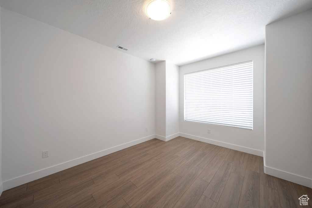 Unfurnished room with baseboards, visible vents, a textured ceiling, and wood finished floors