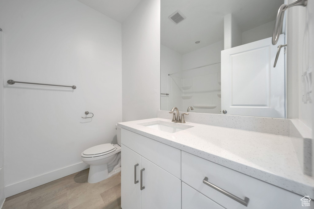 Full bathroom with toilet, visible vents, vanity, wood finished floors, and a shower