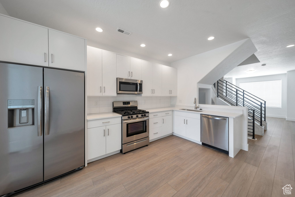 Kitchen with light wood-style flooring, a sink, decorative backsplash, light countertops, and appliances with stainless steel finishes