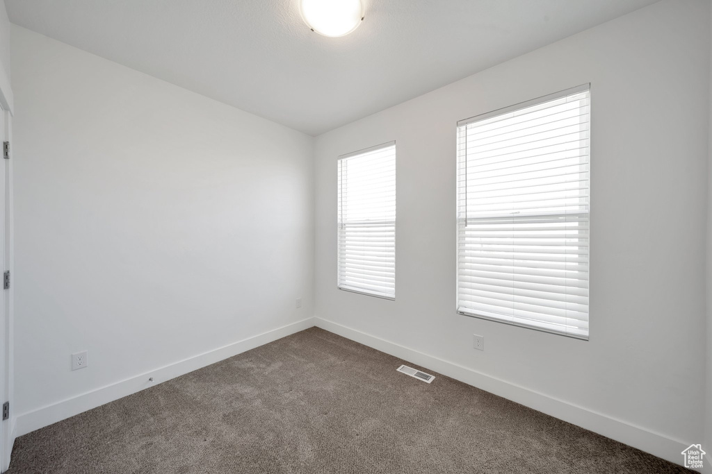 Unfurnished room with visible vents, baseboards, and dark carpet