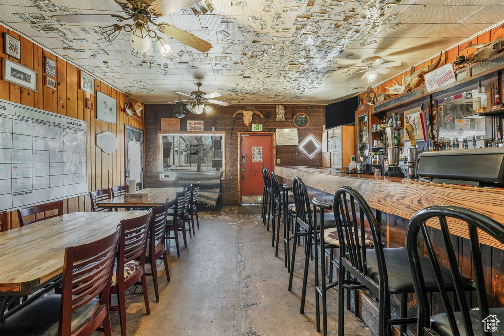 Dining room with wood walls, a ceiling fan, and concrete floors