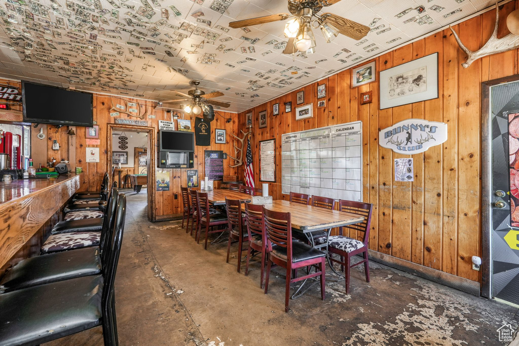 Dining space with unfinished concrete floors, wooden walls, and a ceiling fan