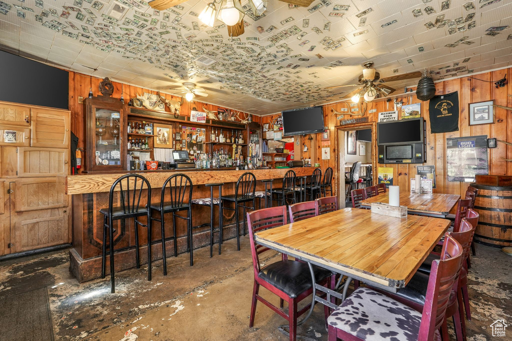 Dining room with a dry bar, wood walls, and a ceiling fan