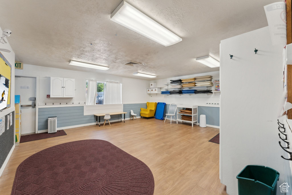 Interior space with wainscoting, a textured ceiling, light wood-type flooring, and visible vents