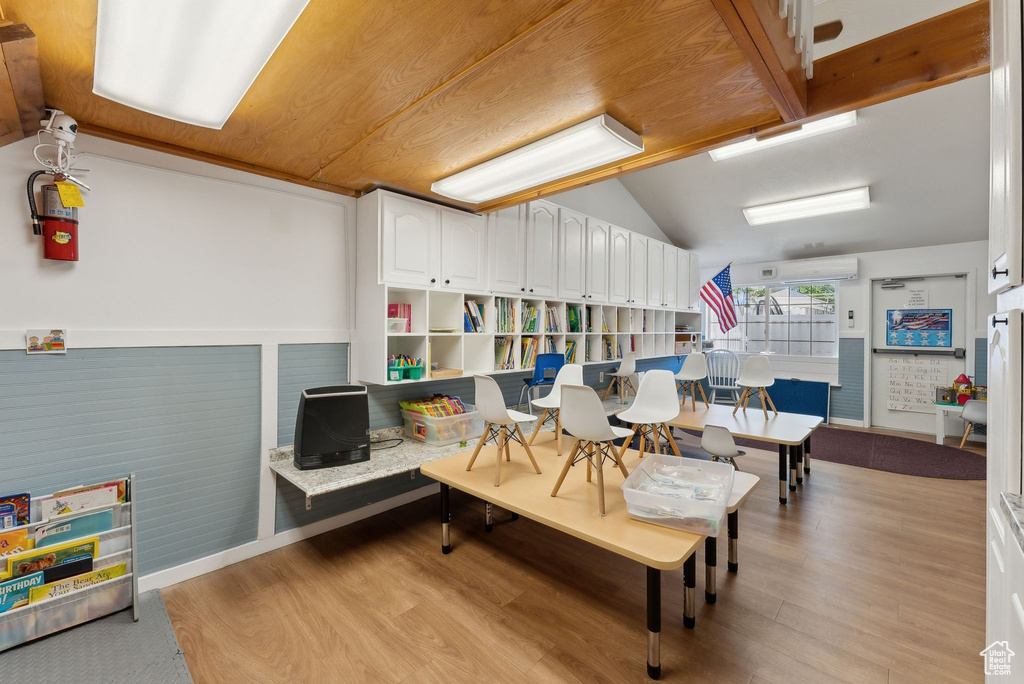 Playroom with light wood finished floors, lofted ceiling, and a wall mounted AC