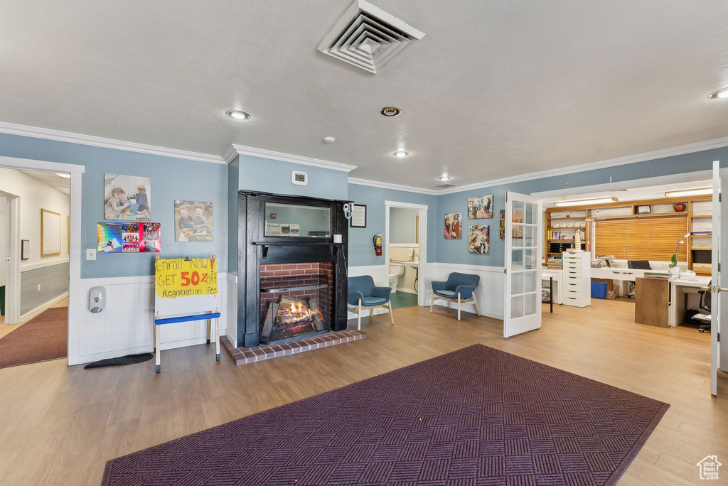Living area featuring wainscoting, visible vents, crown molding, wood finished floors, and a fireplace