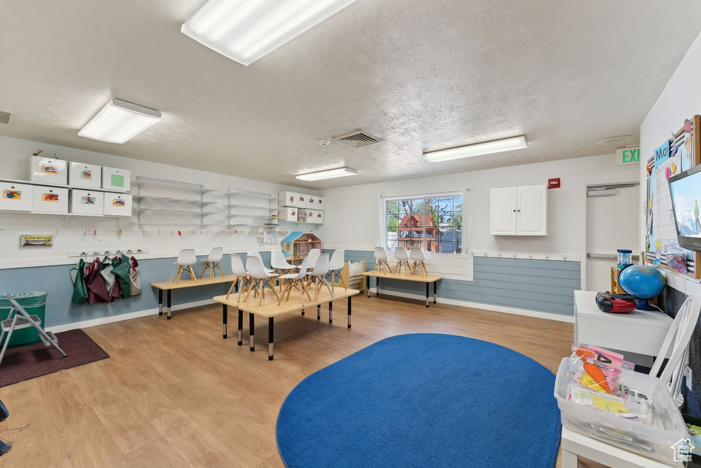 Game room featuring light wood-style flooring, a textured ceiling, a wainscoted wall, and visible vents