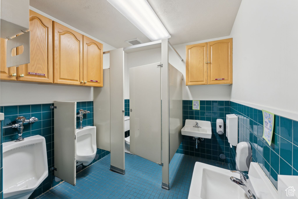 Bathroom with a sink, tile patterned floors, tile walls, visible vents, and wainscoting