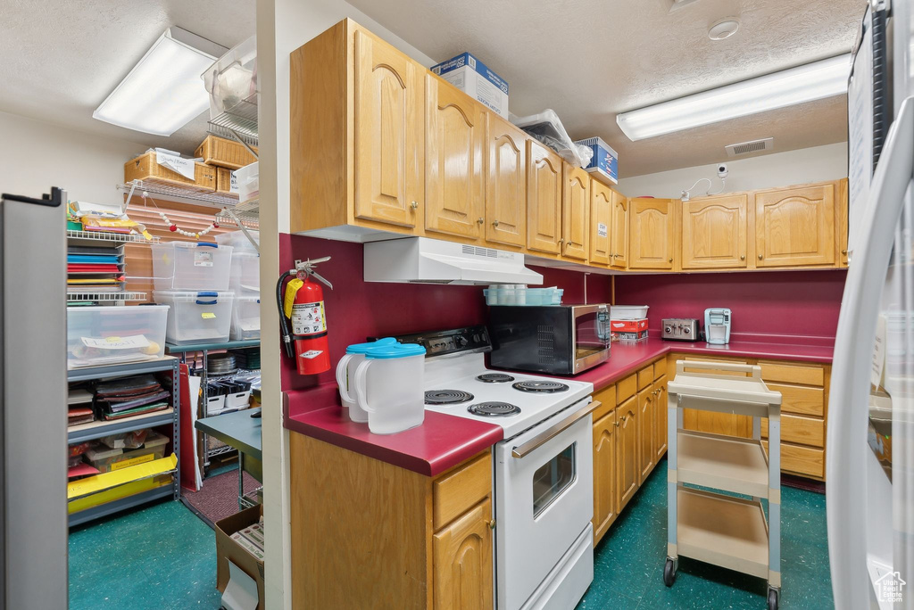 Kitchen featuring light brown cabinetry, visible vents, stainless steel microwave, under cabinet range hood, and white electric range