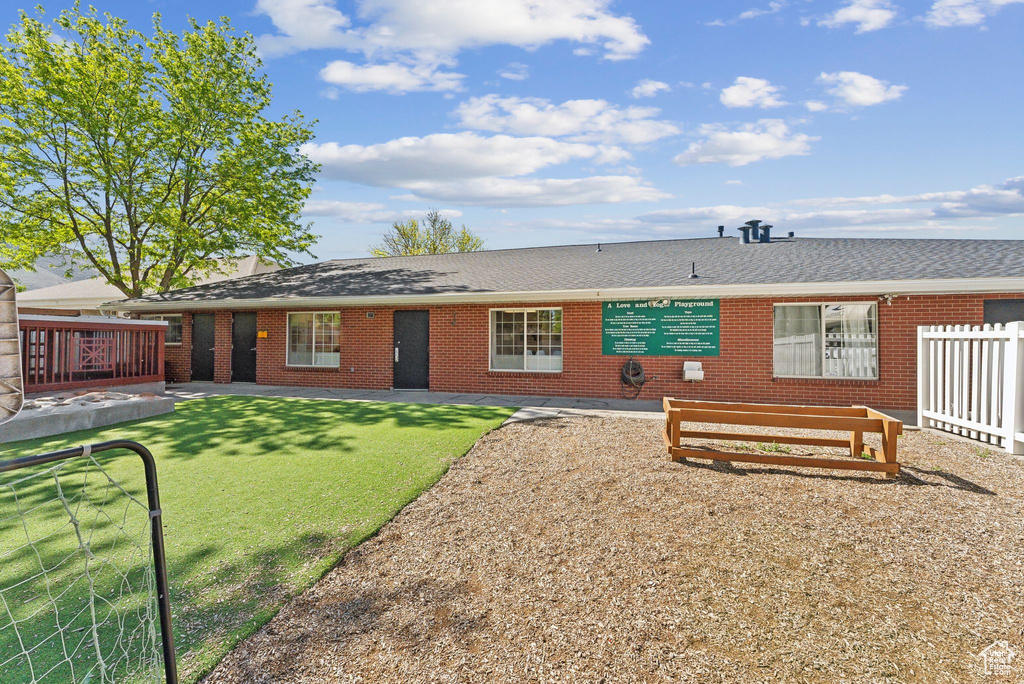 Back of house featuring a yard, roof with shingles, brick siding, and fence