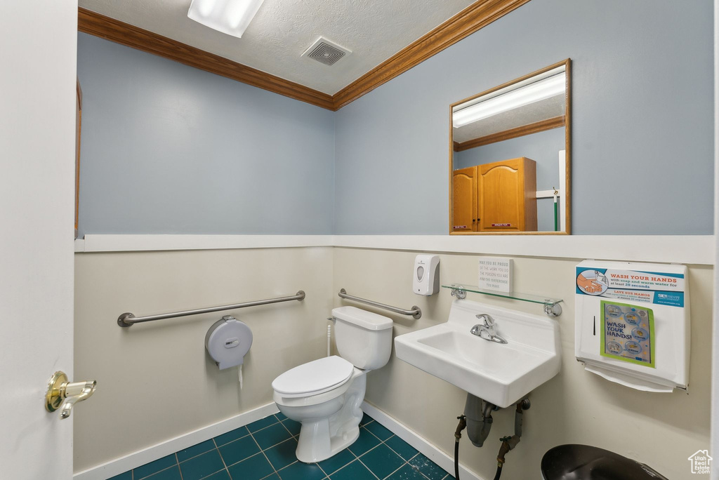 Half bath with a textured ceiling, toilet, ornamental molding, visible vents, and tile patterned floors