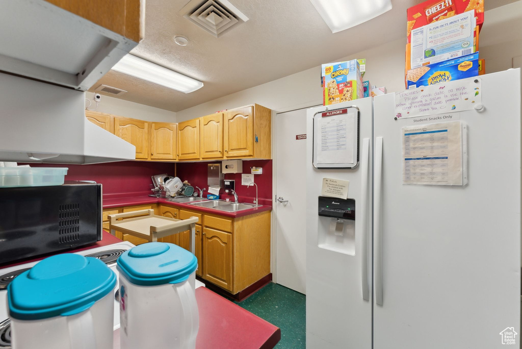 Kitchen with white fridge with ice dispenser, black microwave, visible vents, and a sink