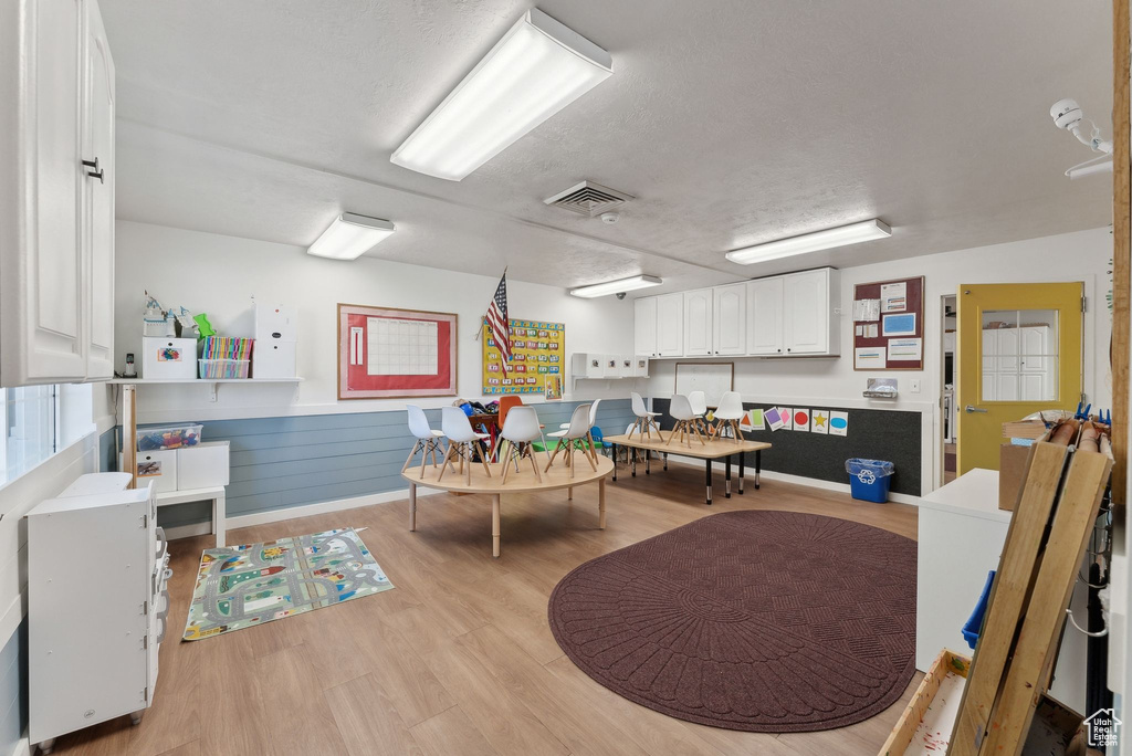 Game room featuring light wood finished floors, a textured ceiling, a wainscoted wall, and visible vents