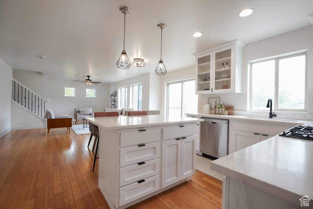 Kitchen featuring stainless steel dishwasher, glass insert cabinets, hanging light fixtures, light countertops, and white cabinets