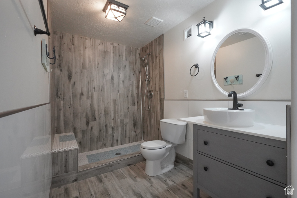Full bathroom with toilet, wood finished floors, vanity, a textured ceiling, and tiled shower