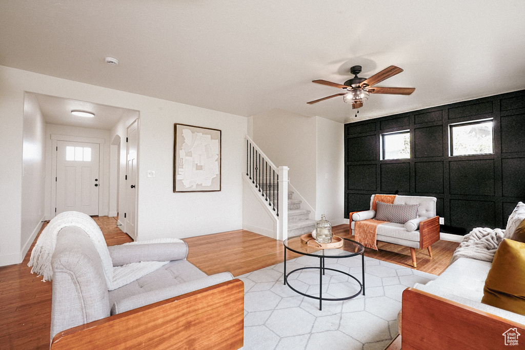 Living area featuring light wood finished floors, stairway, a decorative wall, and a ceiling fan