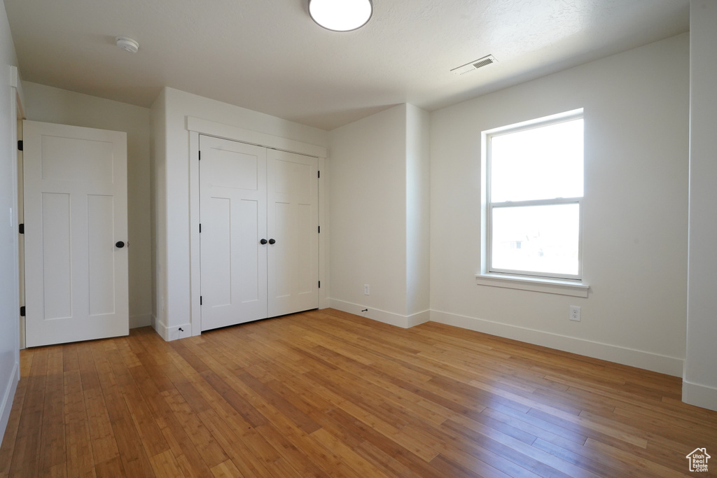 Unfurnished bedroom with a closet, visible vents, light wood-style flooring, and baseboards