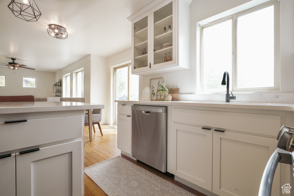 Kitchen with light wood-style flooring, stainless steel dishwasher, ceiling fan, a sink, and light countertops