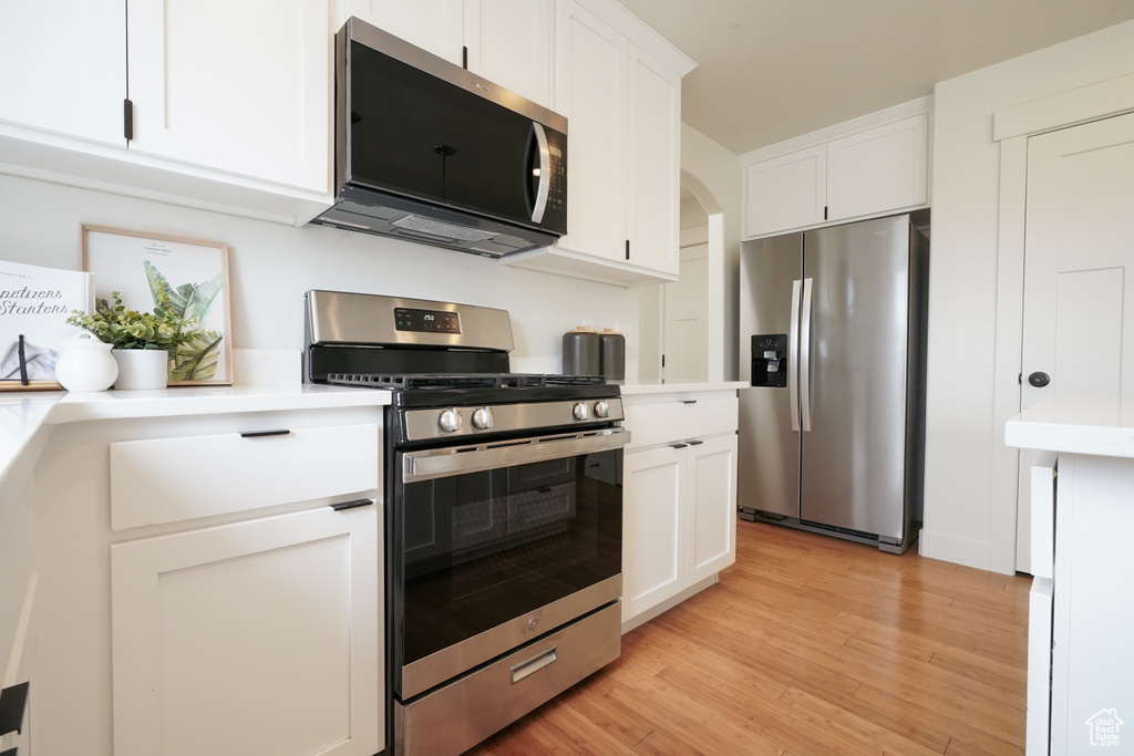 Kitchen with light countertops, white cabinetry, stainless steel appliances, and light wood-style flooring