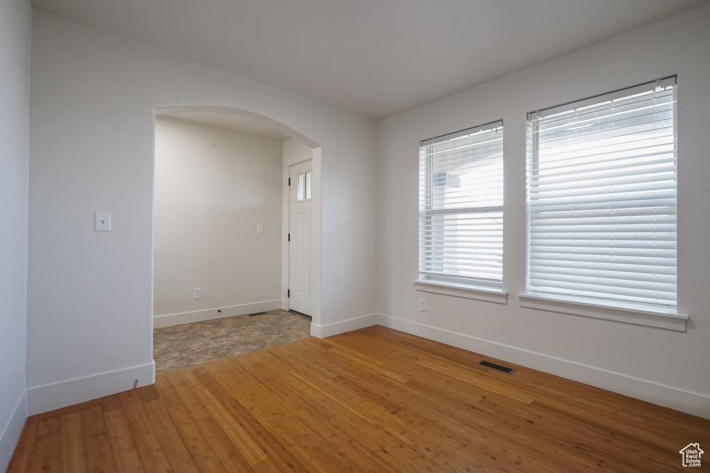 Unfurnished room with baseboards, arched walkways, light wood-type flooring, and visible vents