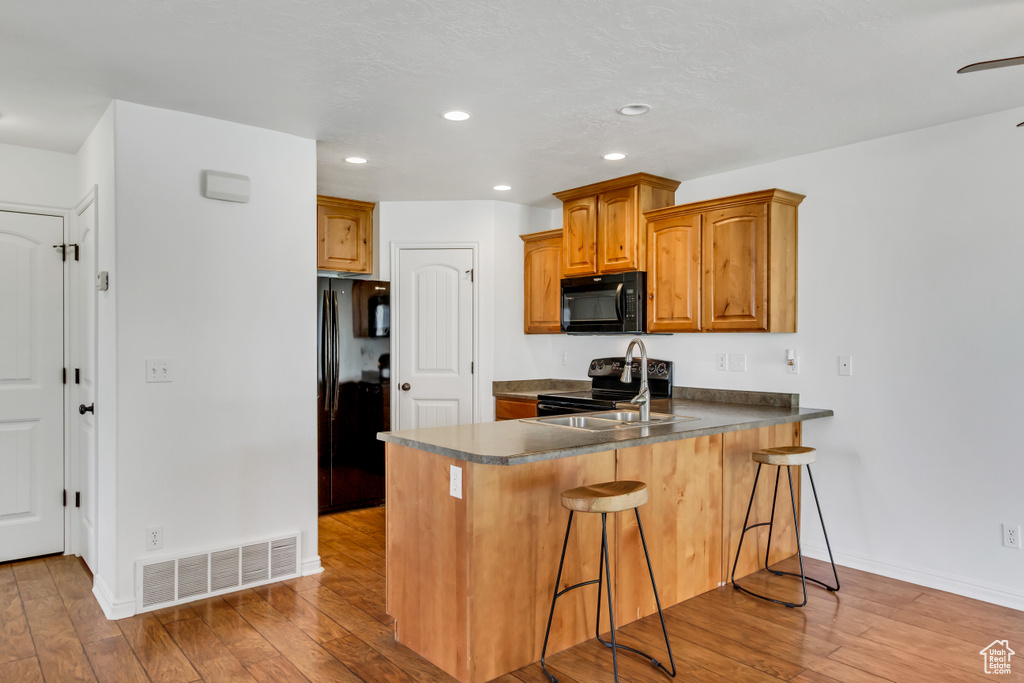 Kitchen with a peninsula, light wood-type flooring, visible vents, baseboards, and black appliances