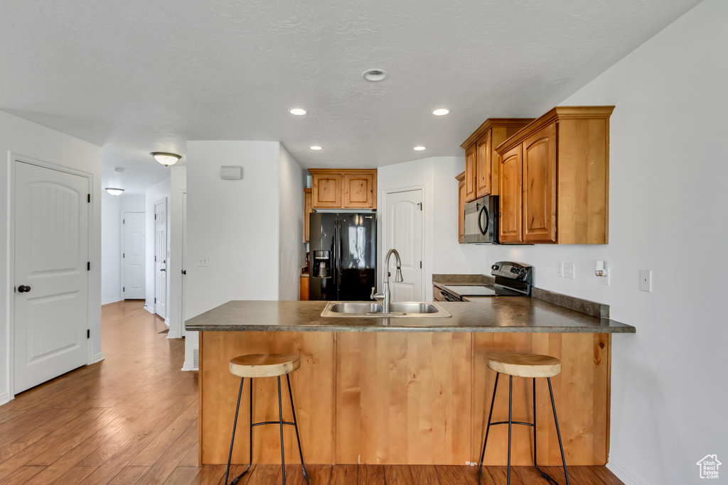 Kitchen with a sink, a peninsula, black appliances, a breakfast bar area, and light wood-style floors