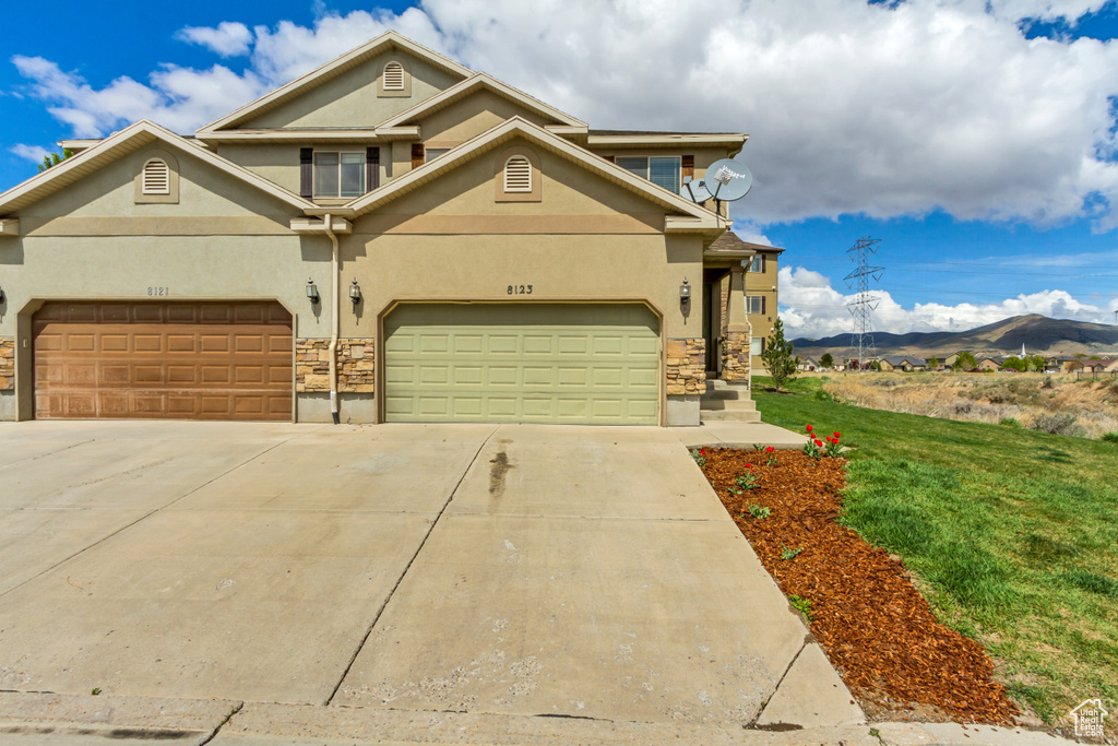 View of front of home featuring a mountain view, a front yard, stucco siding, concrete driveway, and stone siding