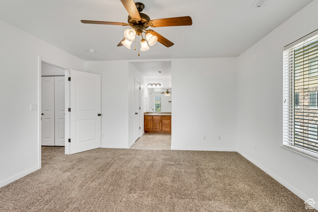 Unfurnished bedroom featuring baseboards, ensuite bathroom, light carpet, and ceiling fan