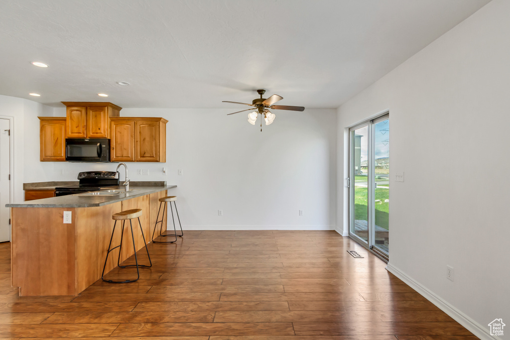 Kitchen with hardwood / wood-style floors, a breakfast bar, black appliances, recessed lighting, and a ceiling fan