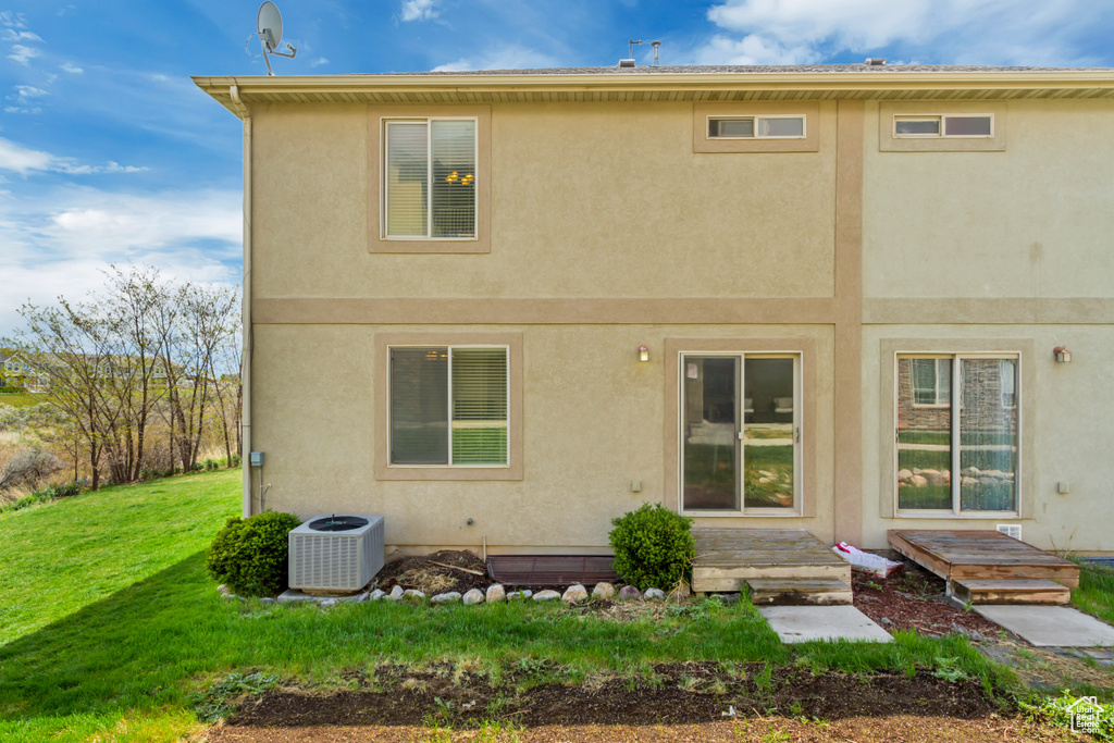 Back of house featuring central air condition unit, a yard, and stucco siding