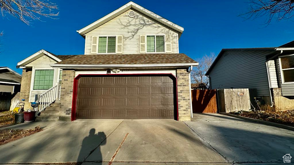 Traditional home featuring concrete driveway, brick siding, an attached garage, and fence