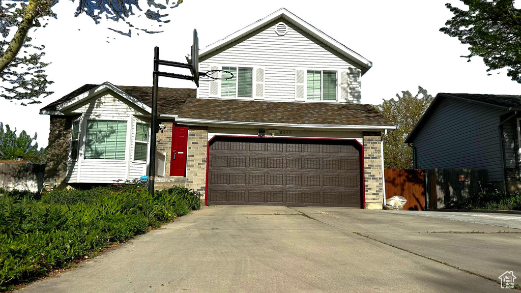 Split level home featuring concrete driveway, brick siding, an attached garage, and fence