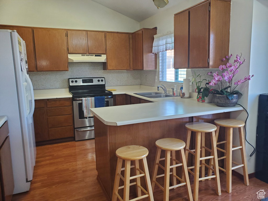Kitchen with a sink, lofted ceiling, under cabinet range hood, electric range, and white refrigerator with ice dispenser