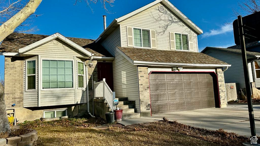 Split level home with concrete driveway, a shingled roof, and a garage