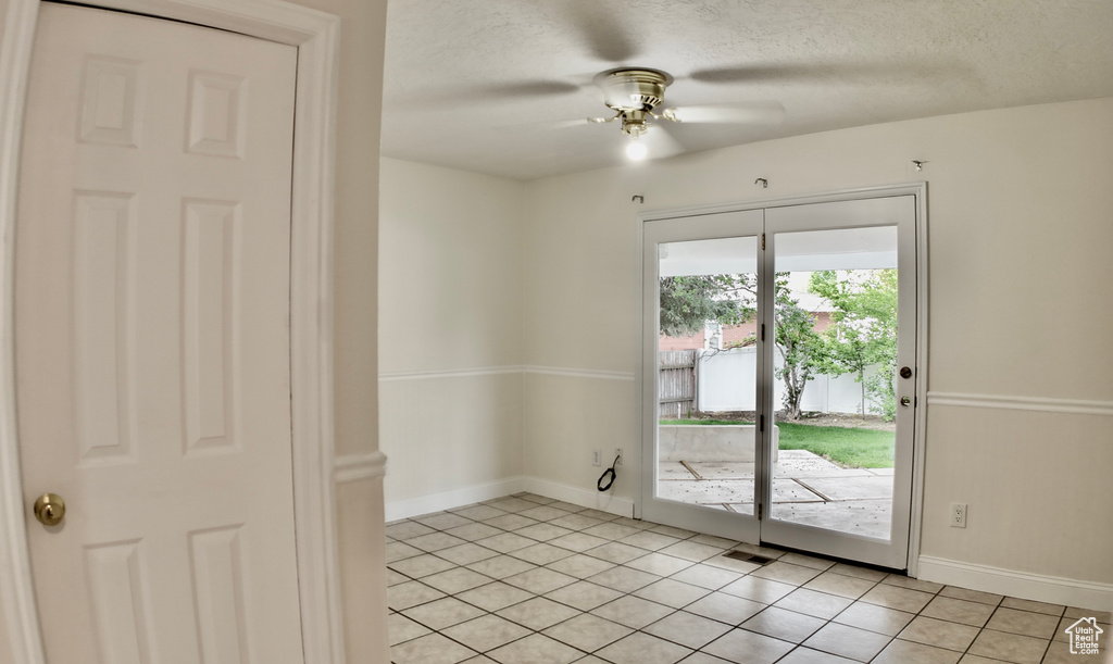 Spare room featuring light tile patterned floors, baseboards, ceiling fan, and a textured ceiling
