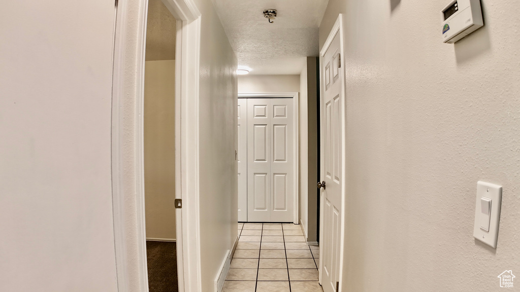 Hall with baseboards, a textured ceiling, and light tile patterned flooring