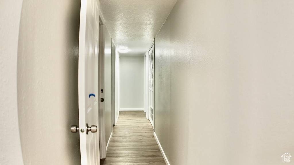 Corridor featuring baseboards, a textured ceiling, and wood finished floors