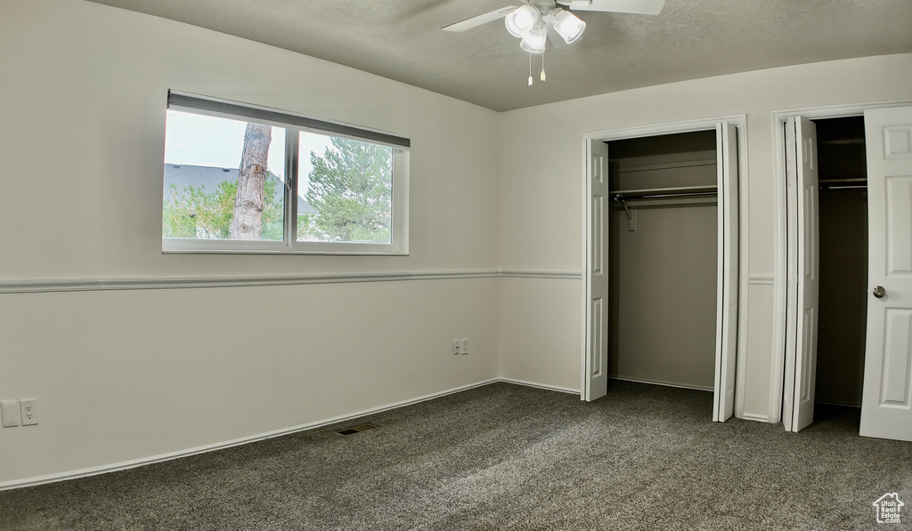 Unfurnished bedroom with dark colored carpet, multiple closets, ceiling fan, and visible vents
