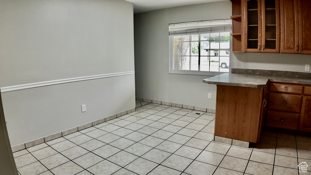 Kitchen featuring dark countertops, open shelves, brown cabinets, light tile patterned floors, and glass insert cabinets